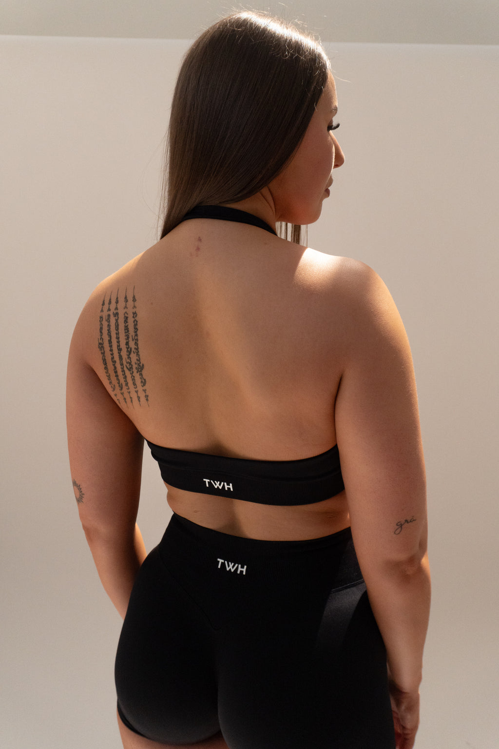 Person wearing a black sports bra and shorts with 'TWH' branding on a plain background
