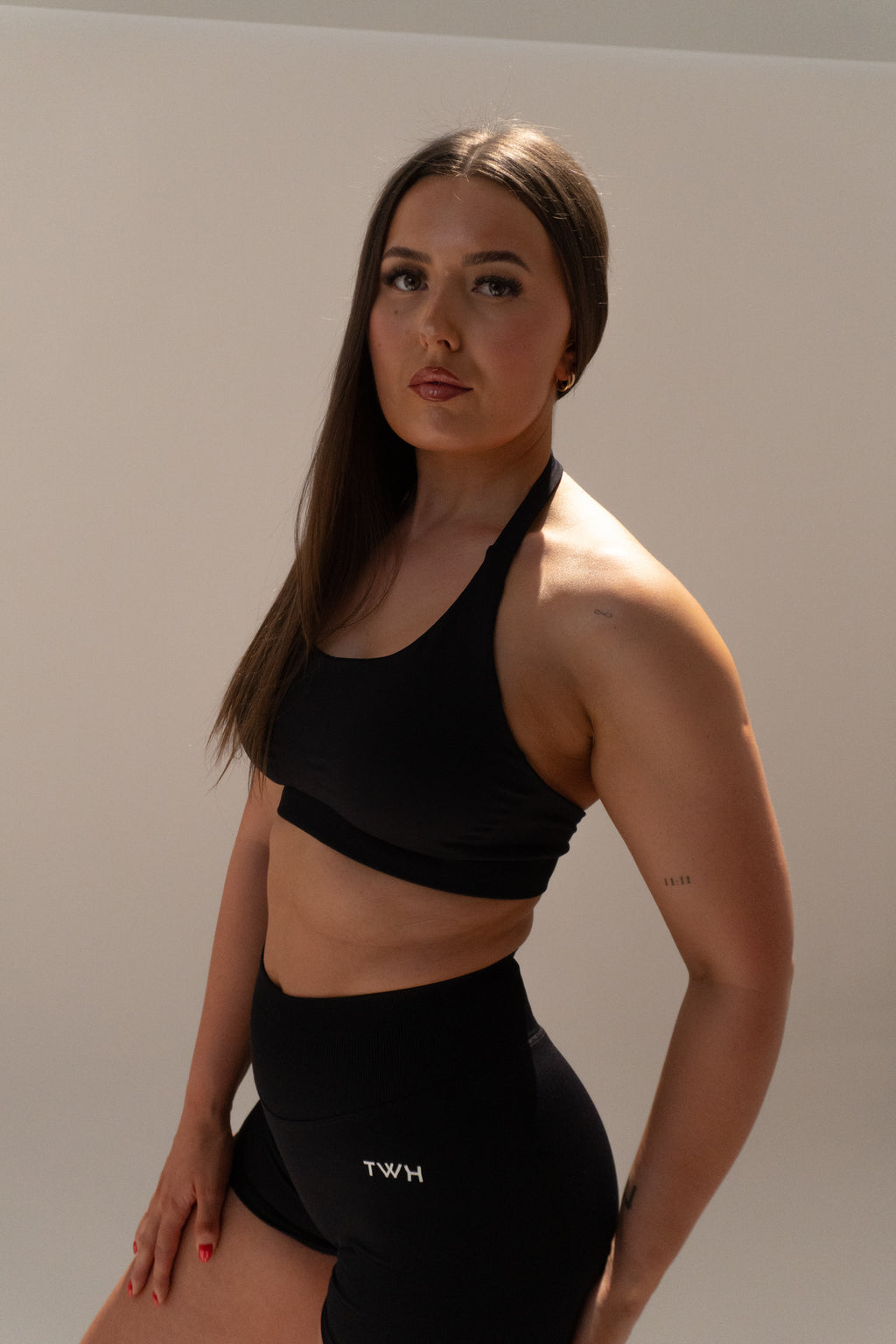 Woman wearing a black sports bra and leggings with 'TWH' branding on a plain background