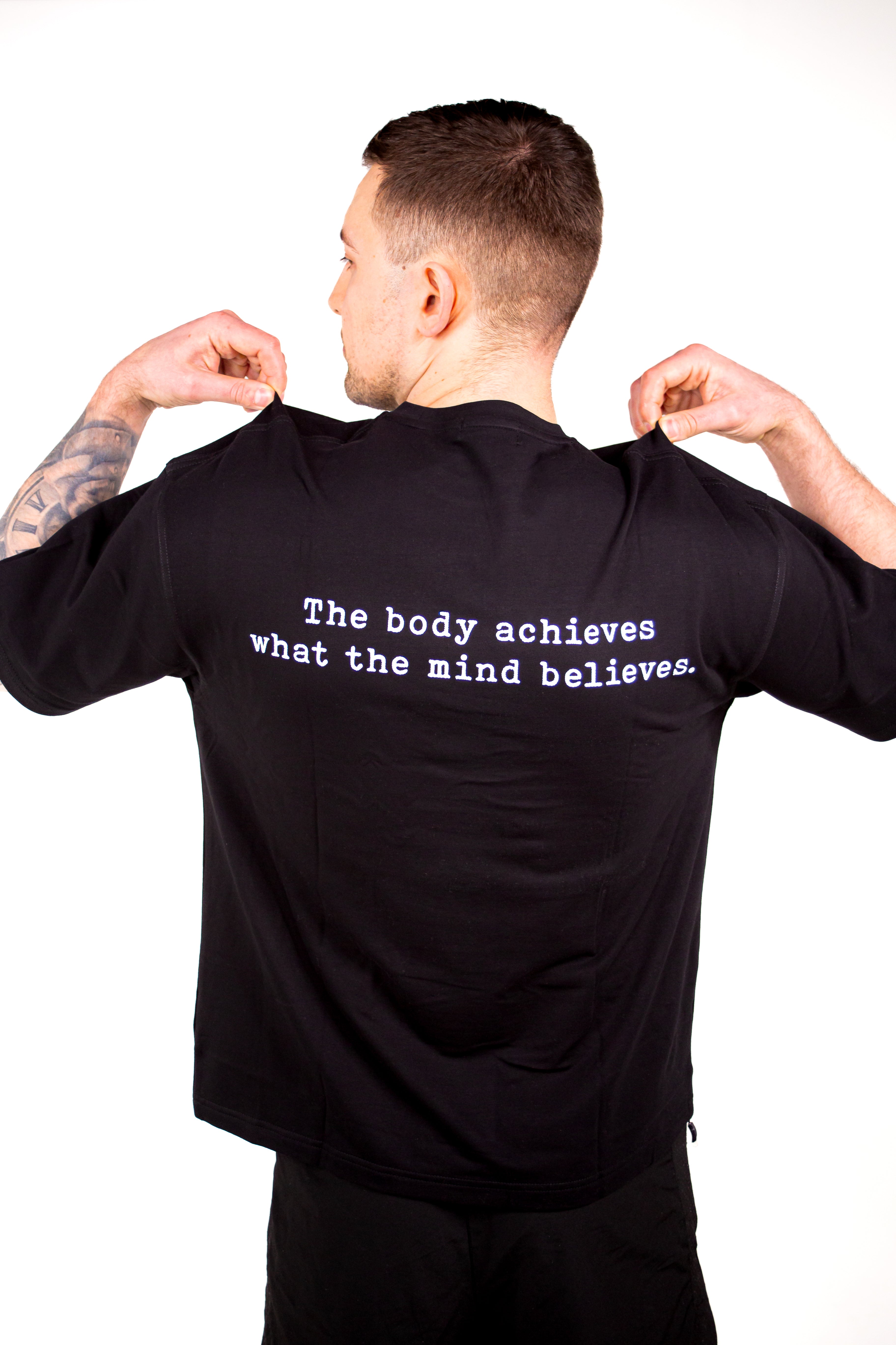 Man wearing a black t-shirt with a motivational quote on the back, standing against a white background.