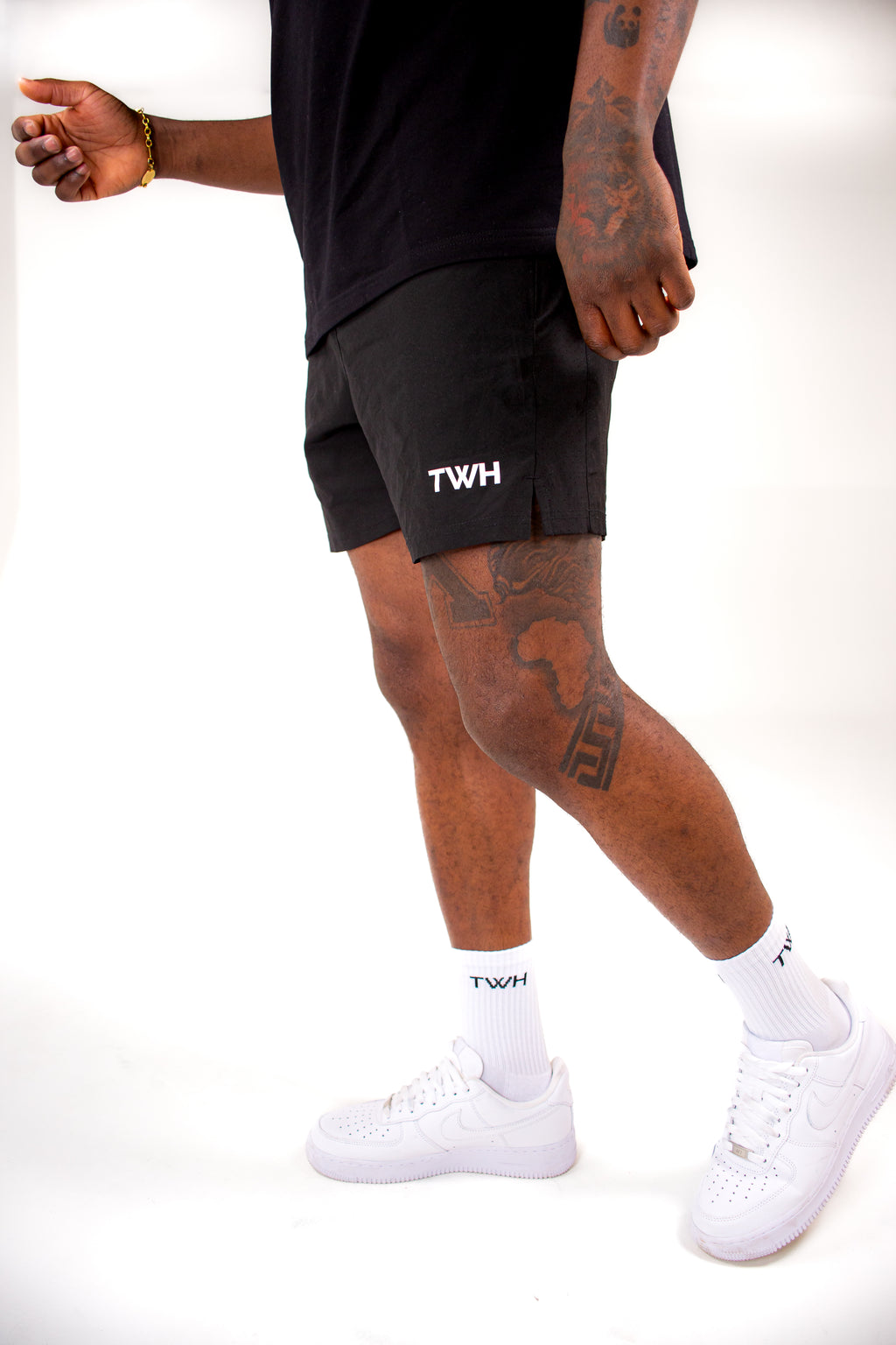 Person wearing black shorts with 'TWH' branding, white sneakers, and socks on a white background
