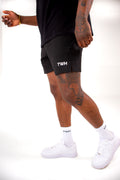 Person wearing black shorts with 'TWH' branding, white sneakers, and socks on a white background