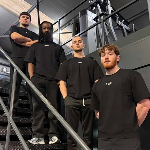 Four men wearing black t-shirts with 'TWH' logo standing on a staircase.
